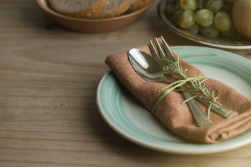Fork and spoon over napkin, with a twig of rosemary. Fruits and bread on background. Healthy food. Rustic wooden background. Food education.