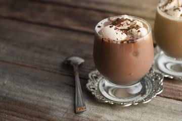 Latte macchiato in a glass with cream on wooden background, decorated withcocoa powder and cinnamon, vintage style. Copy space.