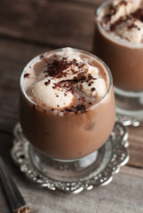 Latte macchiato in a glass with cream on wooden background, decorated withcocoa powder and cinnamon, vintage style.