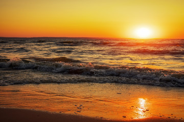 Coast of the sea at dawn. Waves wash the sand. The log lies on the beach. Beautiful time - sunset.