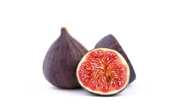 One whole and two halves of ripe common fig fruit. Slowly rotating on the turntable isolated on the white background. Close-up. Macro.