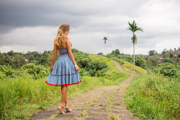 Beautiful young woman in blue vintage dress at stone hill path in Asia look forward. Girl travel and explore world. Long lonely road in mountains. Travel and adventure mockup. Romantic scene concept.
