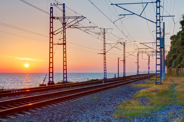 Beautiful landscape of a railroad and towers of traction line on the background of the sea at...