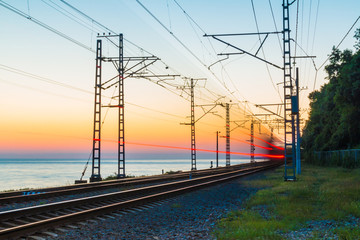 Fototapeta na wymiar Beautiful landscape of a railroad with motion blurred train on the background of the sea at twilight, Sochi, Russia 