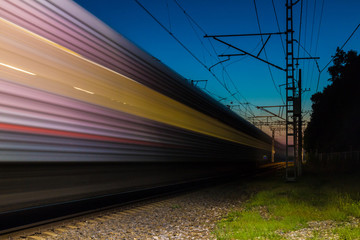 An illuminated railroad with a train in motion blur at dusk, Sochi, Russia
