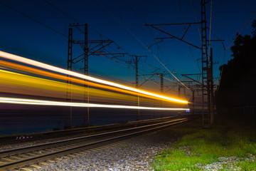 Fototapeta na wymiar An illuminated railroad with light trails of a motion blurred train at dusk, Sochi, Russia 