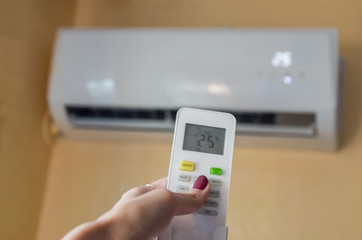 Air conditioner inside the room with woman operating remote controller. / Air conditioner with remote controller