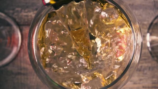 Slow motion from the bottle pour white wine into the glass with the reflection of the other glass top view