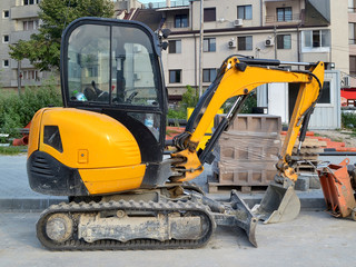 Yellow mini excavator on tracks for small construction works in hard-to-reach places or on narrow city streets, side view, summer day