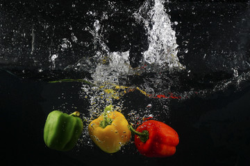 several coloured paprika falling into water splash with many bubble