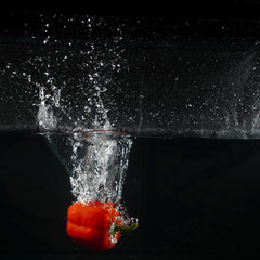 several coloured paprika falling into water splash with many bubble