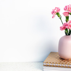 White wall, terrazzo desk and pink vase with carnations standing on notebooks