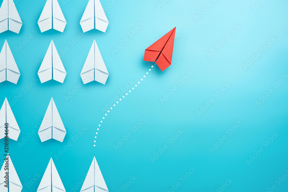 Wall mural group of white paper plane in one direction and one red paper plane pointing in different way on blu