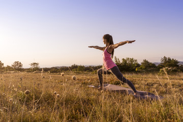 Young beautiful woman practicing Yoga outdoor in nature during sunset