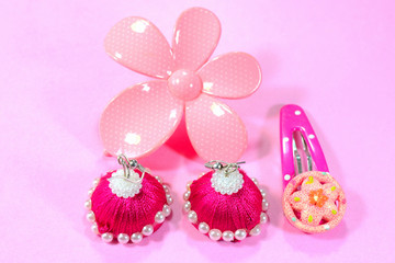 Pink colored ear rings, hair clip and brooch on a pink background.