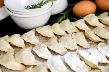 Hand-made pies of white flour lie on a wooden table on a background of white dishes. Vareniki.  Traditional Russian cuisine.