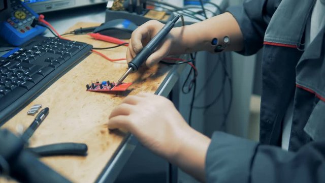 Top view of an artificially-handed workshop employee soldering a circuit