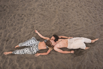 aerial view picture of young cheerful beautiful couple laying down at the beach on the sand. relax and enjoy the summer season in holiday. ethnic and hippy clothes for nice people in vacation