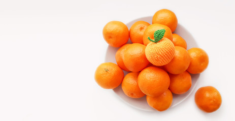 high key.Unique and individuality concept.Mini oranges and clementines whole on porcelain beige plate on white background,closeup top view.One crochet orange on the top of composition.Funny imitation 