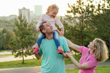 Fototapeta premium active daughter is sitting on his father's neck next mother happy family in the park