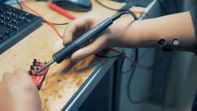 Workshop employee with artificial hands is repairing a microscheme with a soldering tool