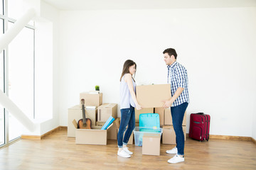 Fototapeta na wymiar Couple Lifting Heavy Cardboard Box While Setting Up New Home