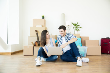 Couple Using Laptop While Sitting On Floor Against Moving Boxes