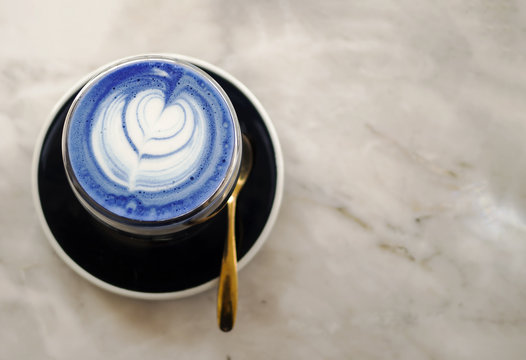 Closeup of hot butterfly pea latte on light marble table background, healthy drink with latte art, morning fresh up