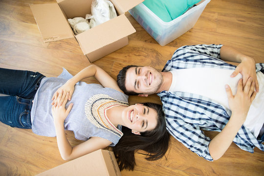 Happy Couple Lying By Boxes On Floor In New Home
