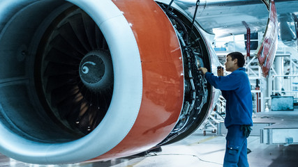 Aircraft maintenance mechanic with a flash light inspects plane engine in a hangar.