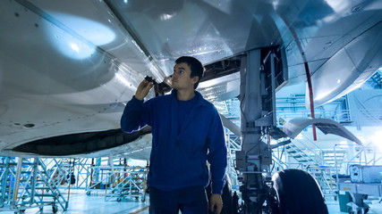 Aircraft maintenance mechanic with a flash light inspects plane fuselage in a hangar.