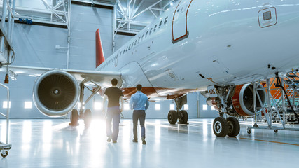 Obraz premium W Hangar Aircraft Maintenance Engineer pokazuje dane techniczne komputera tabletu technikowi samolotowemu. Idą obok czystego, nowego samolotu.