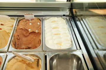 Bar with many flavors of delicious ice cream for sale. Fridge with creamy vanilla, white chocolate, nescafe irish ice cream tastes in serving steel container. Sweet dessert with decorating elements.