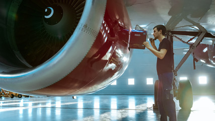 In a Hangar Aircraft Maintenance Young Engineer/ Technician/ Mechanic With Tablet Computer Inspects...