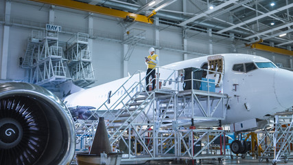 Obraz premium Inżynier w zbawczej kamizelki pozyci obok samolotu w hangarze