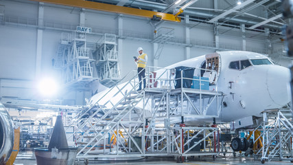 Engineer in Safety Vest Standing next to Airplane in Hangar