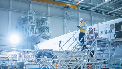 Engineer in Safety Vest Standing next to Airplane in Hangar