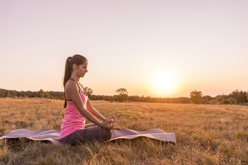 Young beautiful woman practicing Yoga outdoor in nature during sunset