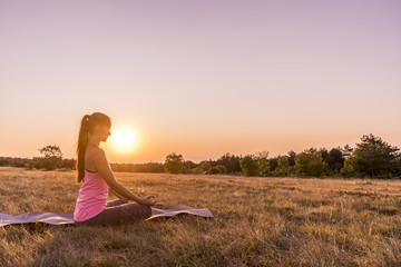 Young beautiful woman practicing Yoga outdoor in nature during sunset