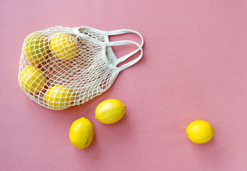 Mesh shopping bag with lemons on pink canvas background.