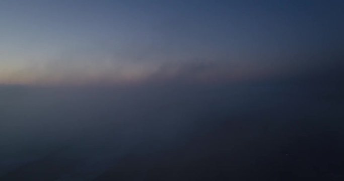 Aerial flight through fog with beach and ocean below.