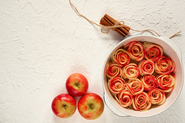 Аpple pie in the baking dish decorated with fresh apples and cinnamon sticks. Vegetarian tart on the white background. Delicious autumn dessert. Top view with copy space for text