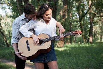 young couple walking in the forest, playing guitar and dancing, summer nature, bright sunlight, shadows and green leaves, romantic feelings