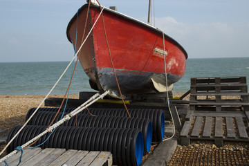 Red fishing boat on a beach (with all names removed) with the sea behind it and steps made from...