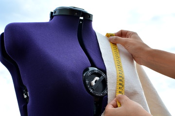 Mujer trabajando tomando medidas con una cinta métrica sobre un trozo de tela colocado en un maniquí de modista realizando un diseño de moda