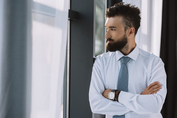 Fototapeta premium bearded businessman with crossed arms looking at window in office