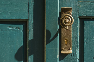 alter Türknauf aus Messing mit Griff in Schleifenform an grüner Holztür, old brass door knob with looped handle on green wooden door