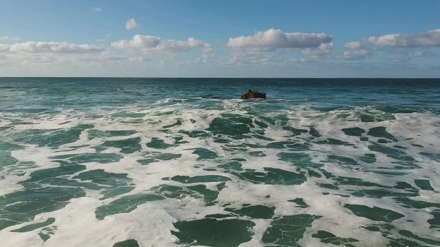 Backwards drone shot hovering over coastal wave coming to shore in Waimea Beach, Hawaii.