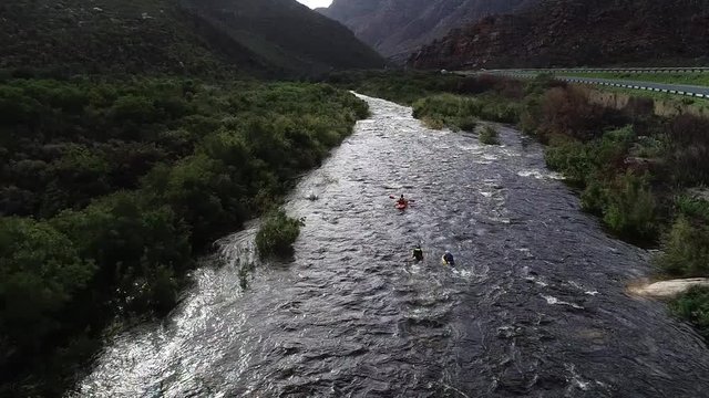Aerial footage of white water kayaks paddling in the white water rapids on a freestone stream in the western cape of south africa during a winter storm.