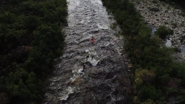 Aerial footage of white water kayaks paddling in the white water rapids on a freestone stream in the western cape of south africa during a winter storm.